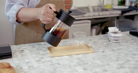 Asian senior barista pouring freshly brewed tea into glass cup on counter inside coffee shop during retirement business showing warm hospitality and preparation care