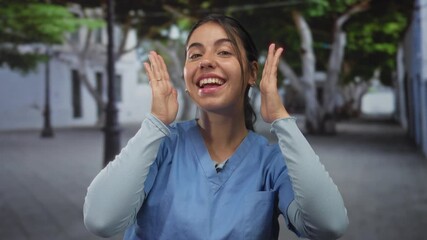 Young hispanic woman framing her smiling face with both hands on busy street; playfulness creativity curiosity.