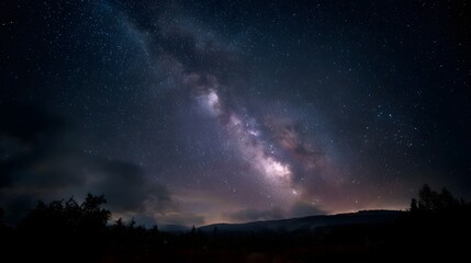 Fototapeta premium The Milky Way galaxy illuminates a dark silhouetted landscape under a vast starry night sky