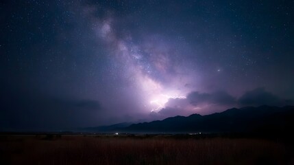 Lightning strike illuminates the Milky Way galaxy above a dark mountain range and grassy field at night