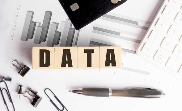 Data written on wooden blocks with financial charts, credit card, pen and office supplies on white desk