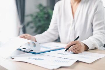 A businesswoman analyzes financial charts and reports with pen while reviewing documents on clipboard at office desk. Concept of accounting, business planning, data analysis and corporate strategy.