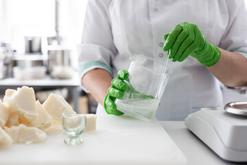 A laboratory technician in a white coat and green nitrile gloves stirs a liquid in a beaker. Сraft...