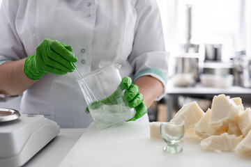 A laboratory technician in a white coat and green nitrile gloves stirs a liquid in a beaker. Сraft...