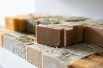 Various bars of handmade, cold-process soap are curing on a shelf. These organic cosmetics feature different natural ingredients, resulting in beige, green, yellow, and purple colors.