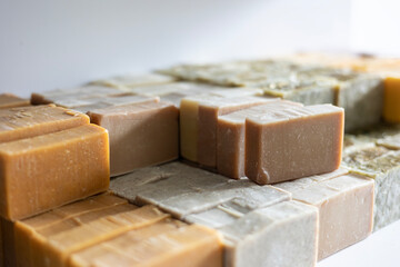Various bars of handmade, cold-process soap are curing on a shelf. These organic cosmetics feature different natural ingredients, resulting in beige, green, yellow, and purple colors.