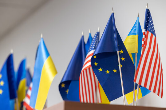 A close-up view of the small table flags of Ukraine, the USA, and the European Union. This display symbolizes international partnership, diplomacy, and support for Ukraine.