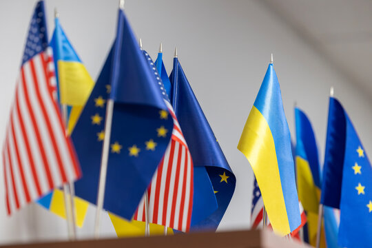 A close-up view of the small table flags of Ukraine, the USA, and the European Union. This display symbolizes international partnership, diplomacy, and support for Ukraine.