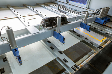 A high-angle view of an automated panel-saw in a woodworking factory. This industrial machine, with its motor and rollers, cuts large MDF or chipboard panels to precise sizes.