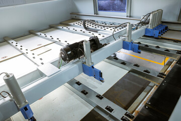 A high-angle view of an automated panel-saw in a woodworking factory. This industrial machine, with its motor and rollers, cuts large MDF or chipboard panels to precise sizes.