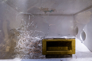 A close-up of the waste collection chamber inside an edge banding machine. A pile of thin plastic edge band trimmings and shavings sits next to the metal inlet.