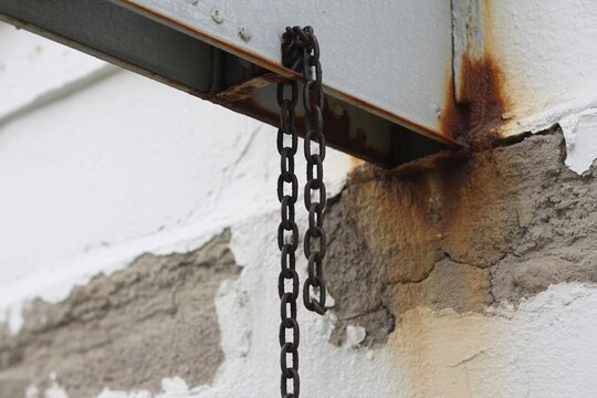 Rusty chain hanging from metal beam against peeling wall industrial decay photo