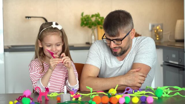 Father and little daughter sit at table and make diy from chenille wire toys. Happy family create handmade craft. Leisure