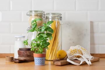 Zero waste kitchen concept with wooden utensils, glass jars and eco mesh bag on wooden table in bright minimalist home interior