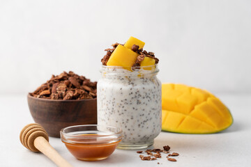 Mango chia pudding in glass jar and chocolate granola on light background with copy space. Healthy breakfast concept