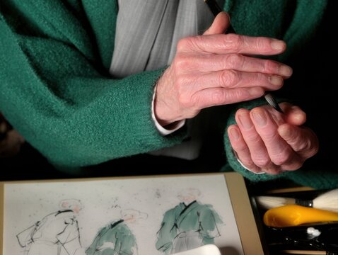 Delicate hands of a Japanese calligrapher gracefully hold a brush over parchment, showcasing the elegance of calligraphy in progress.