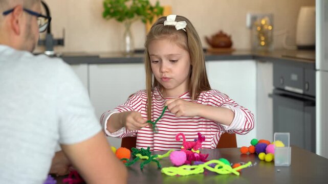 Father helps little daughter create handmade craft. Happy little girl make diy from chenille wire toys. Family leisure