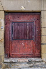 Aged and Weathered Red Wooden Door with Metal-Framed Window Cover and Stone Facade Detail