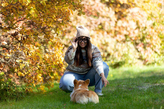 A young woman sits in a park with her pet. A smiling girl enjoys the autumn scenery.