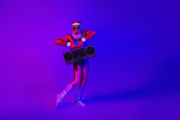 Naklejka premium Elderly man in retro gym outfit with boombox under purple blue neon lights posing for a fitness themed stock image
