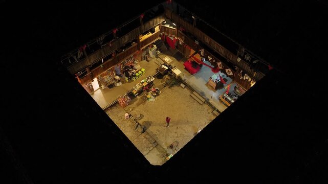 Aerial view of the square Tulou building with a single person in the courtyard, lit by warm yellow light, Fujian, China.