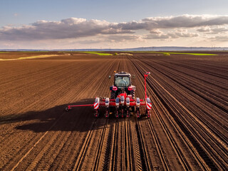 Tractor sowing seeds in ploughed agricultural field at sunset