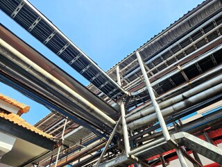 Industrial pipes and cable trays against a blue sky, showing a complex network of infrastructure.