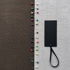 Neatly aligned vibrant pushpins create a visual boundary between rich brown and light grey textile backgrounds, featuring a sleek black blank label for design