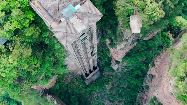 Aerial view of the towering Bailong Elevator rising dramatically amidst the verdant, rugged landscape, a modern marvel contrasting with the natural beauty, Zhangjiajie, China.