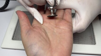 Callus removal with electric nail drill during professional manicure procedure, close-up of hands in gloves female palm treatment
