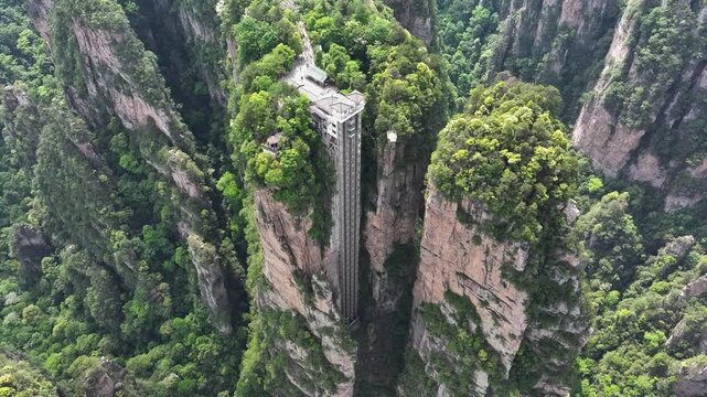 Aerial view of the Bailong Elevator rising through the stunning jagged mountain peaks surrounded by lush green forest, Zhangjiajie, China.