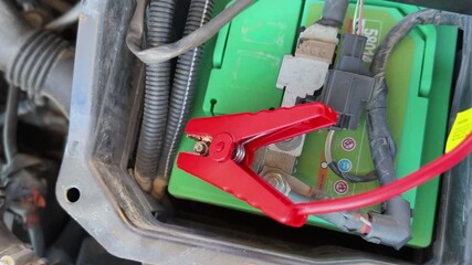 red jumper cable clamp connected to car battery terminal. Ideal for automotive repair, power, maintenance, and emergency service tutorial videos.