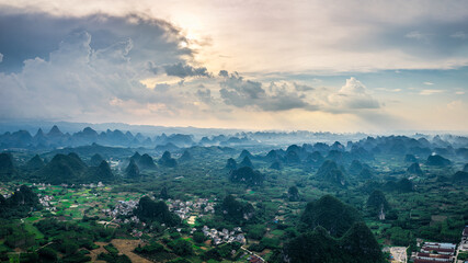 Panorama of unique karst mountain formations and rural villages under a dramatic cloudy sky in Guilin.