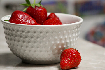 Red ripe strawberries in a textured white bowl with one berry on the table, symbolizing freshness, simplicity, and healthy eating.