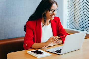Professional woman in a red blazer working on a laptop computer