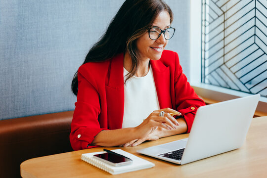 Fototapeta Professional woman in a red blazer working on a laptop computer