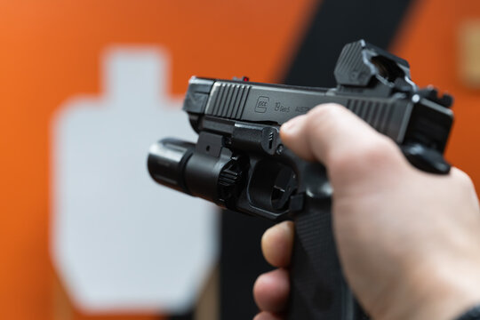 Baltics, November 5, 2025: A hand holding a Glock 19 Gen 5 pistol, equipped with a red dot sight and a tactical flashlight, at an indoor shooting range with a silhouette target in the background.