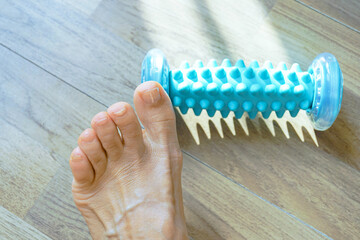 Close-up of a foot and a spiked roller massager on the floor. A woman prepares to perform exercises beneficial for lymphovenous insufficiency, chronic swelling, and flat feet. Home physiotherapy, 
