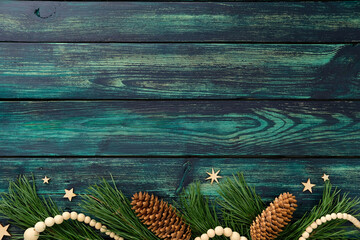 Rustic teal wooden background with pine branches, pinecones, and natural festive decor at bottom,...