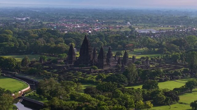 Aerial View of the Prambanan temple complex shrouded by verdant trees and the distant city skyline creating a scene, Yogyakarta, Daerah Istimewa Yogyakarta, Indonesia.