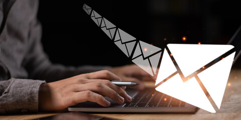 A digital communication concept showing a person typing on a laptop with glowing email icons, representing online messaging, email marketing, and business communication technology.