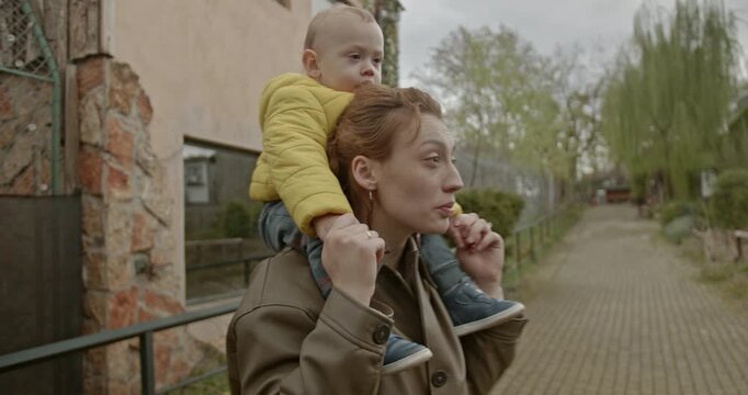 A mother carries her young child on her shoulders as they stroll through the zoo. They enjoy the sights and sounds of the animals. The love between mother and son is clear.