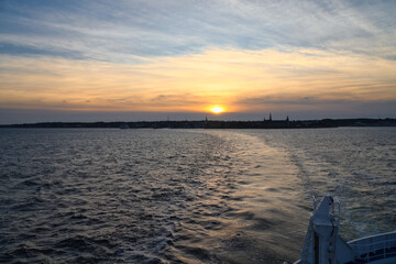 Sunset over the sea with boat trail and silhouette on the horizon