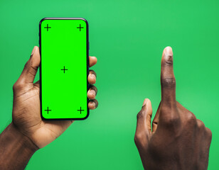 Hand holding smartphone with green screen and finger pointing on green background.