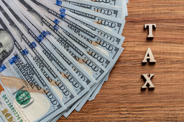 Wooden letters with the inscription tax and $100 American paper bills on table, top view, closeup. Tax text with money dollars on wooden background