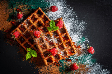 Fresh baked chocolate Belgian waffles with red raspberries and jam on black plate for breakfast, closeup, top view. Culinary, cooking, bakery concept. Food recipe background. Sweet waffles with berry