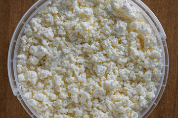 White cottage cheese or fresh milk curd in a plastic container, closeup, top view. Homemade cottage cheese texture