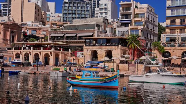 Sliema waterfront in Malta, Sliema, shows a luzzu and a white boat moored by sandstone arches and terrace cafes, people seated outdoors, gentle ripples in late morning light