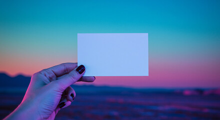 A hand holds a blank white business card against a beautiful sunset sky with pink and blue gradients. A creative and inspiring mockup for modern branding.