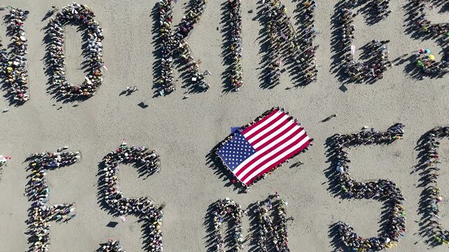 San Francisco, United States - 25 October 2025: Aerial view of crowds forming "NO KINGS YES ON 50" with a US flag, casting shadows on the concrete ground.
